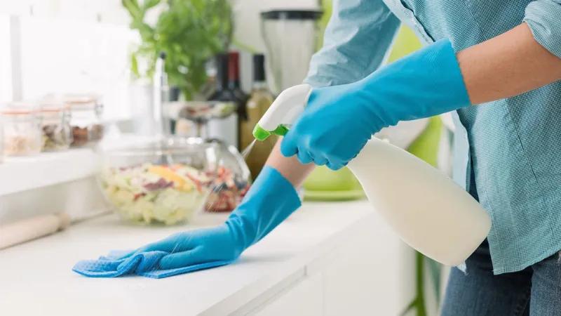 Một người đang đeo khẩu trang và găng tay bảo hộ, cẩn thận đổ bột Cloramin B đã cân vào nước để pha dung dịch 2% cho mục đích khử trùng mạnh.